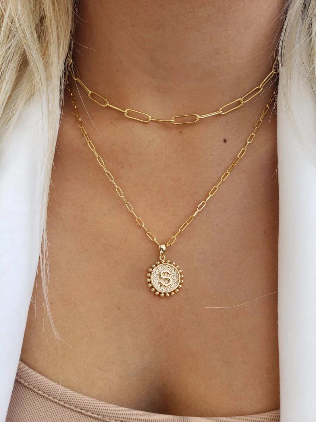 A layered paperclip initial necklace worn with a white shirt